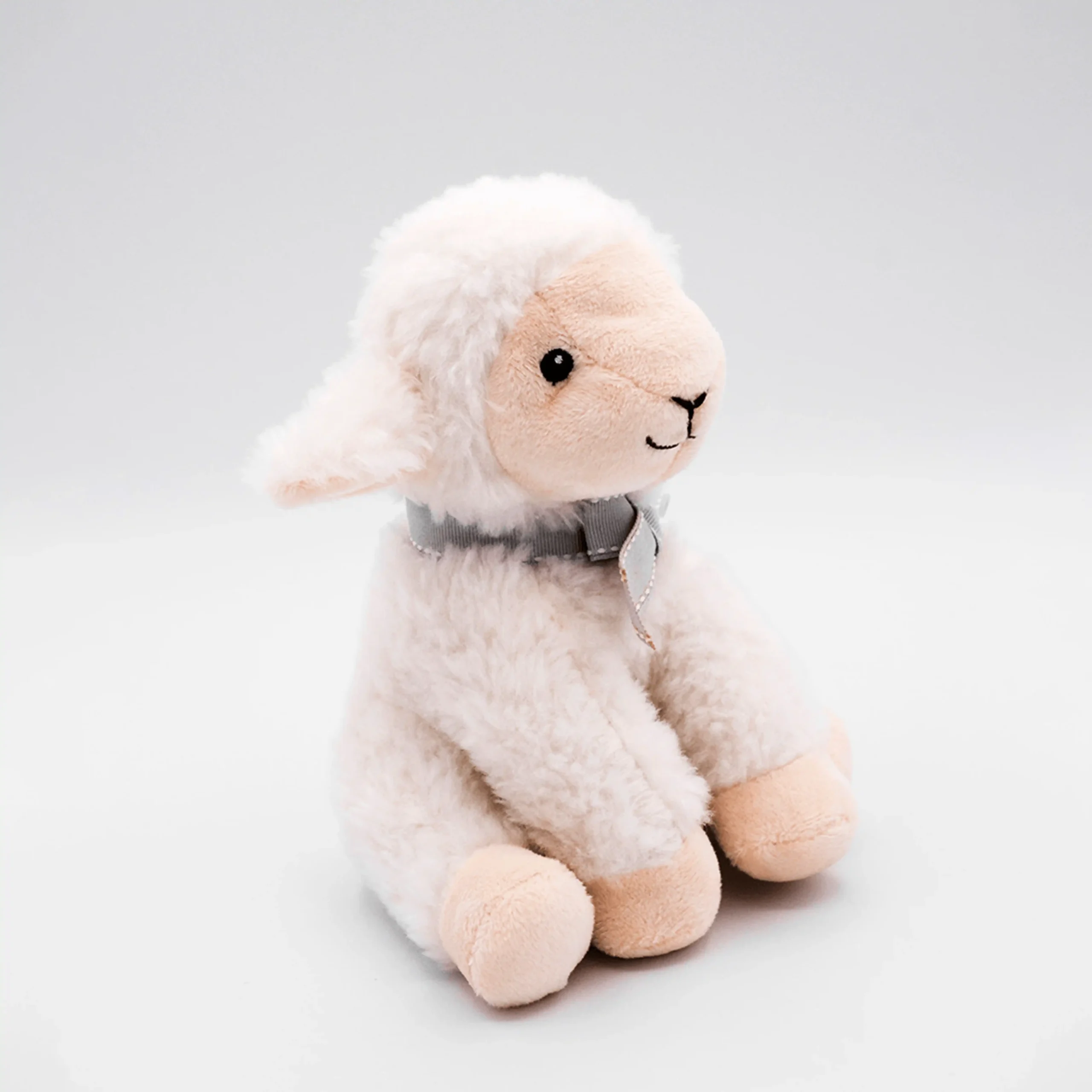 Peluche de corderito blanco con lazo gris visto de perfil sobre fondo blanco