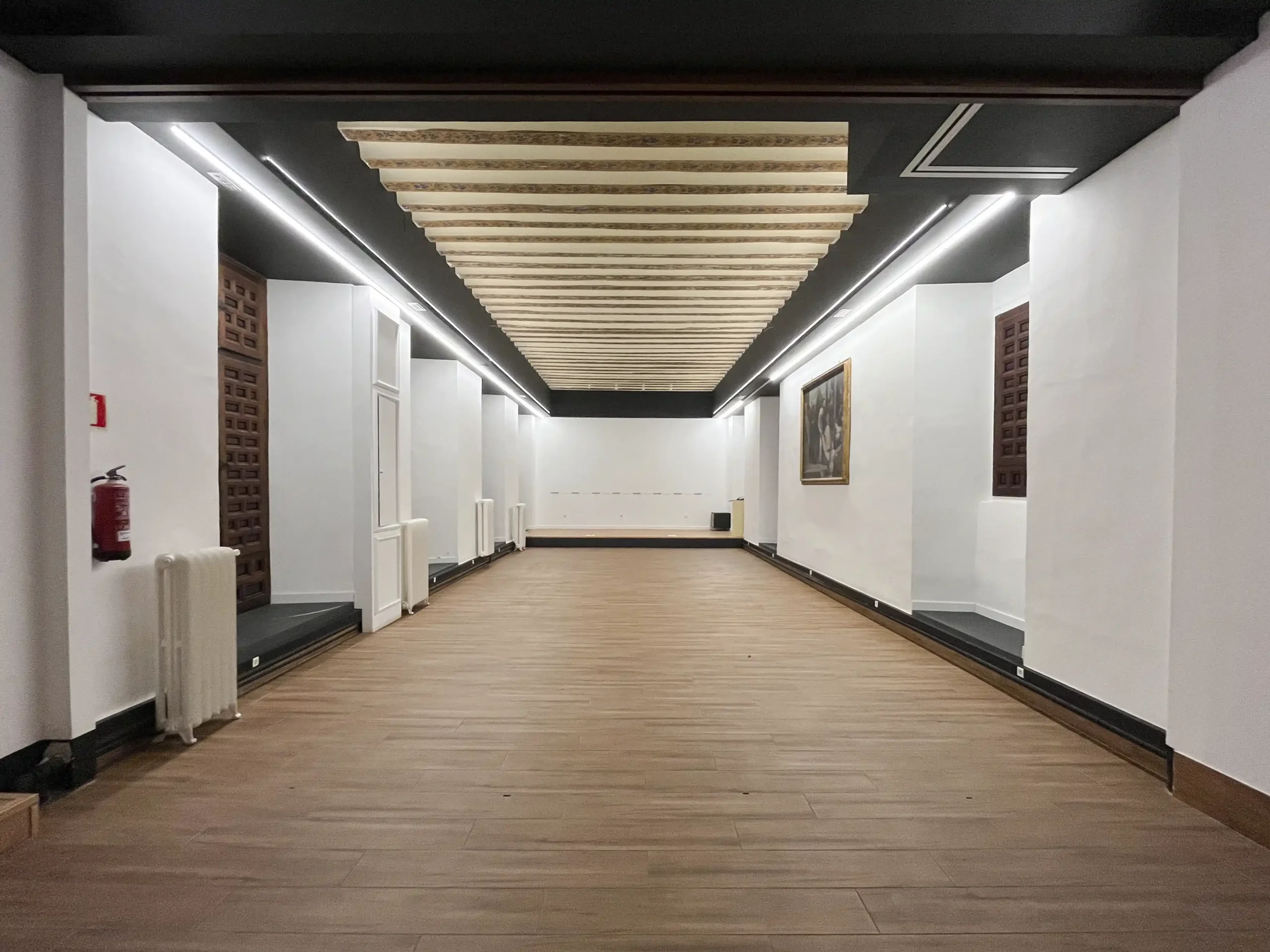 Auditorio del Palacio Episcopal de Segovia, sala diáfana con suelo de madera, techo decorado y luz ambiental.