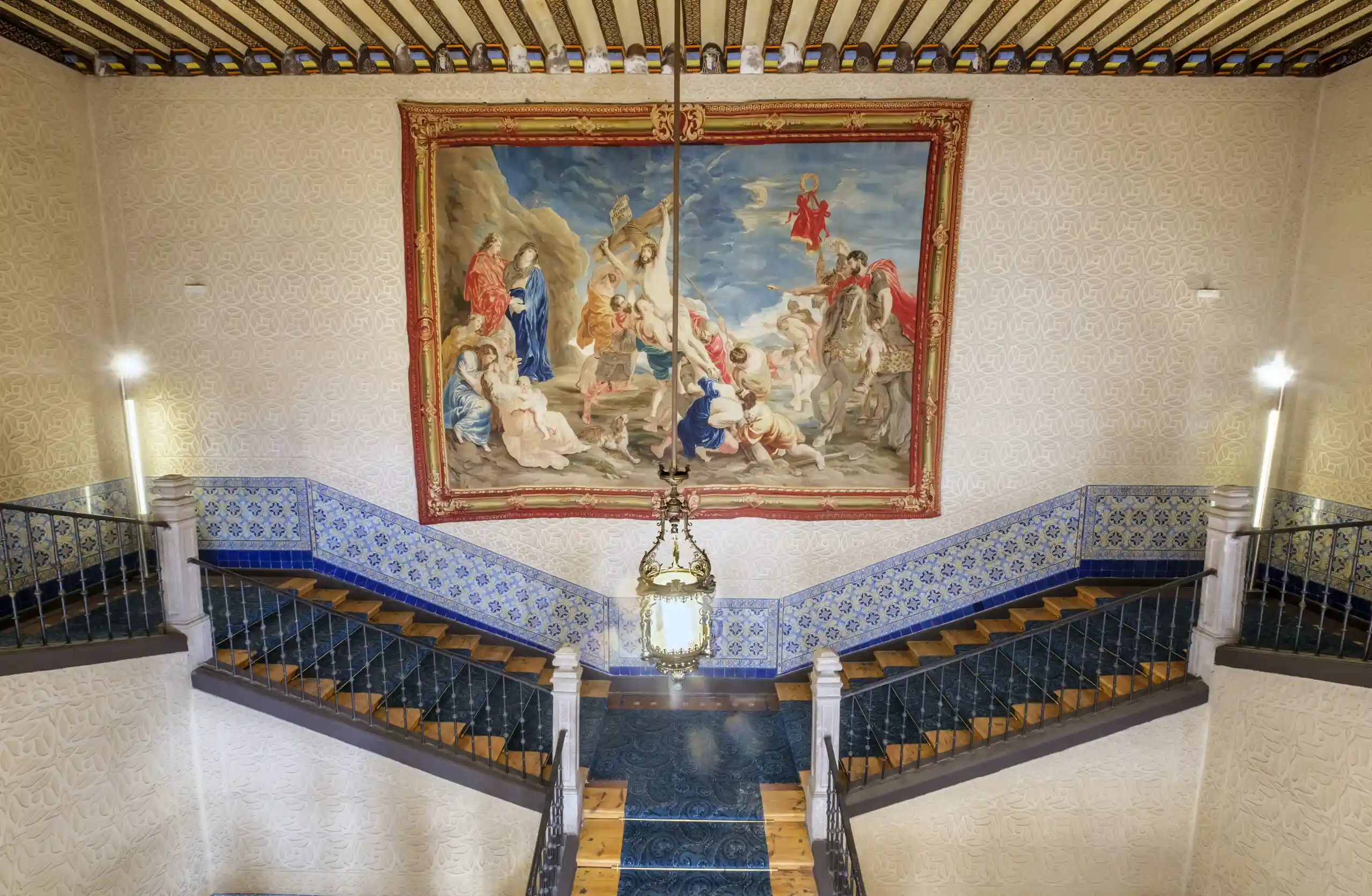 Escalera imperial del Palacio Episcopal de Segovia con esgrafiado, cerámica, artesonado y el tapiz “Elevación de la cruz” inspirado en Rubens, espacio ceremonial para invitados.