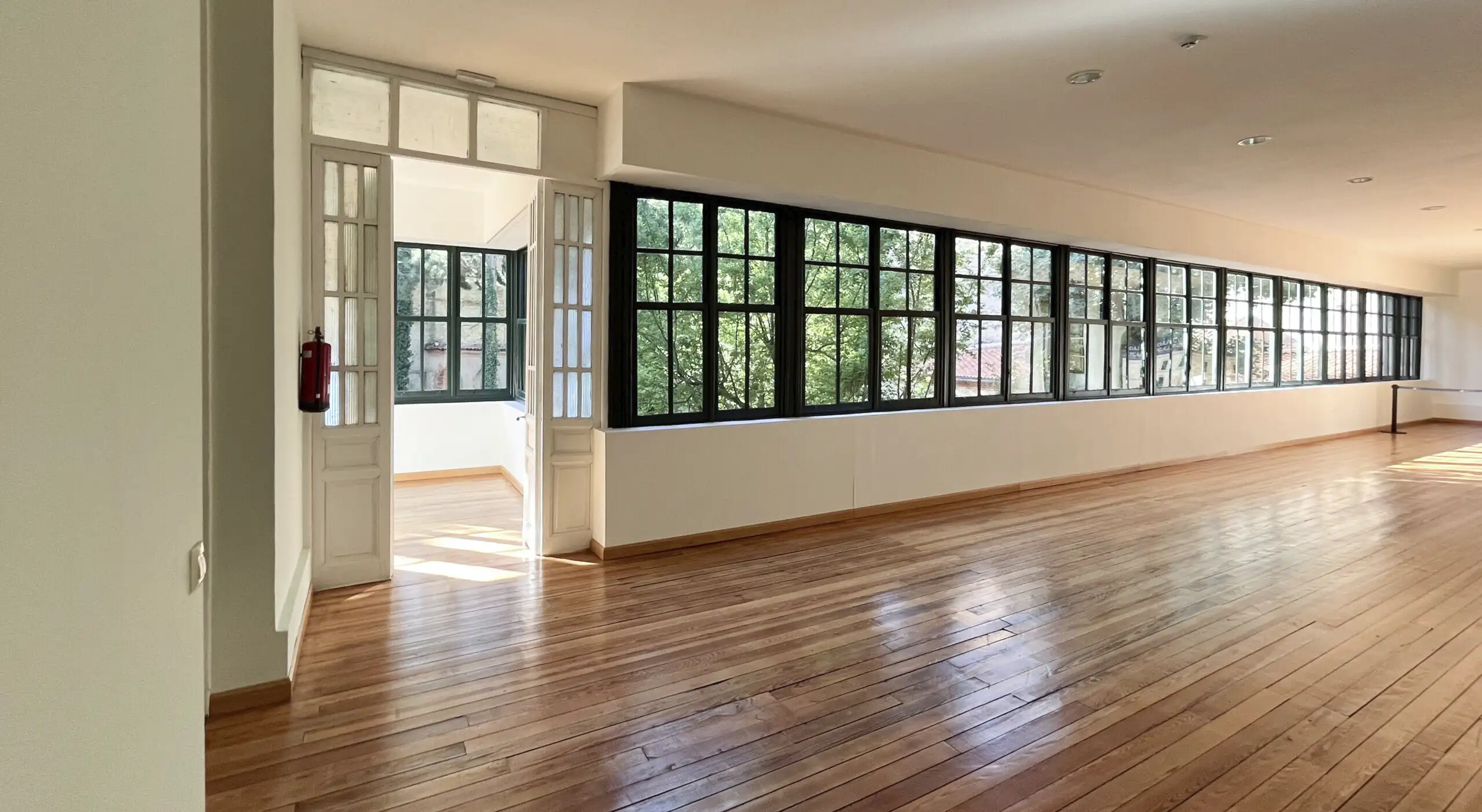 Espacio interior luminoso del Palacio Episcopal de Segovia con grandes ventanales y suelo de madera, ideal para eventos relajados con vistas al jardín.