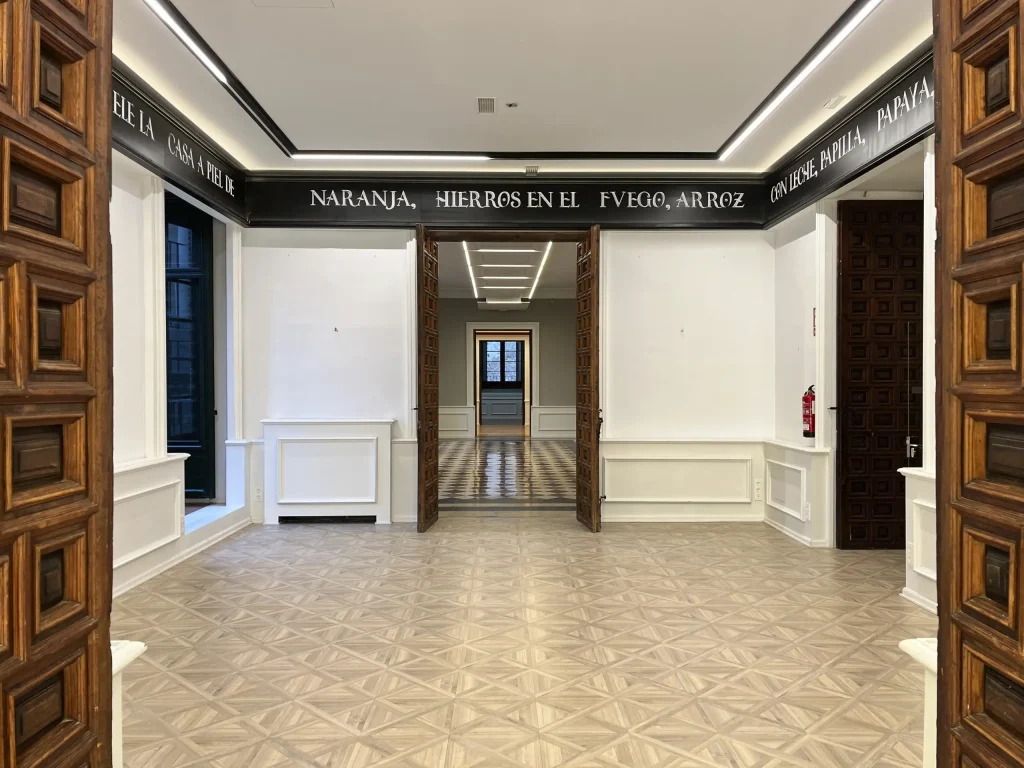 Espacio diáfano con frases en friso, puertas monumentales y suelo geométrico, perfecto para exposiciones o eventos culturales