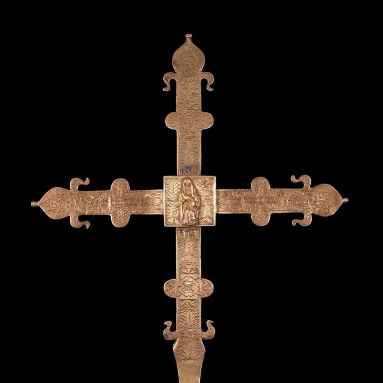 Cruz procesional de bronce del siglo XIV con grabados religiosos y florales, destacando la Virgen María en el centro, expuesta en el Palacio Episcopal de Segovia.
