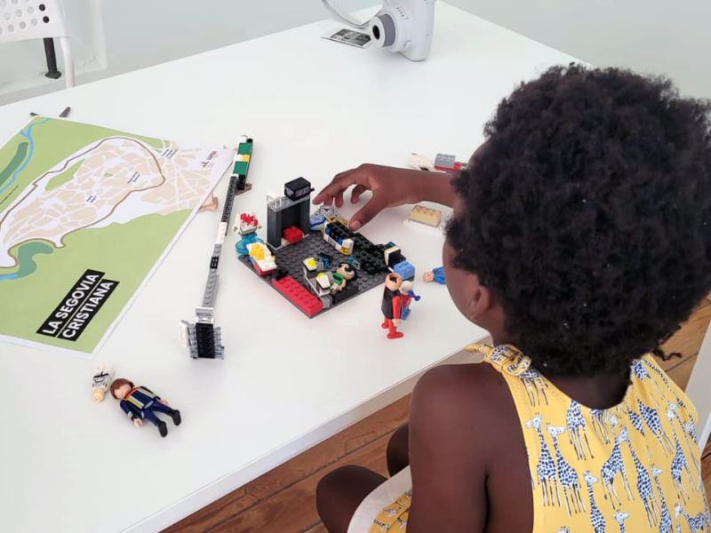 Niña participando en un taller infantil en el Palacio Episcopal de Segovia, jugando con construcciones de Lego y un mapa de "La Segovia Cristiana"